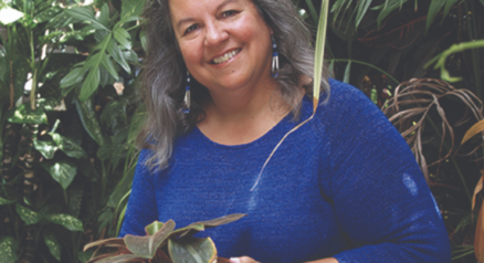 Photo of Robin Wall-Klimmerer in a blue sweater holding a potted plant